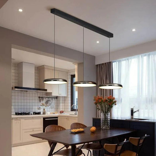 Moderne schwarze Pendelleuchte über einem Esstisch in einer minimalistischen Küche mit Fenster und Küchenutensilien.